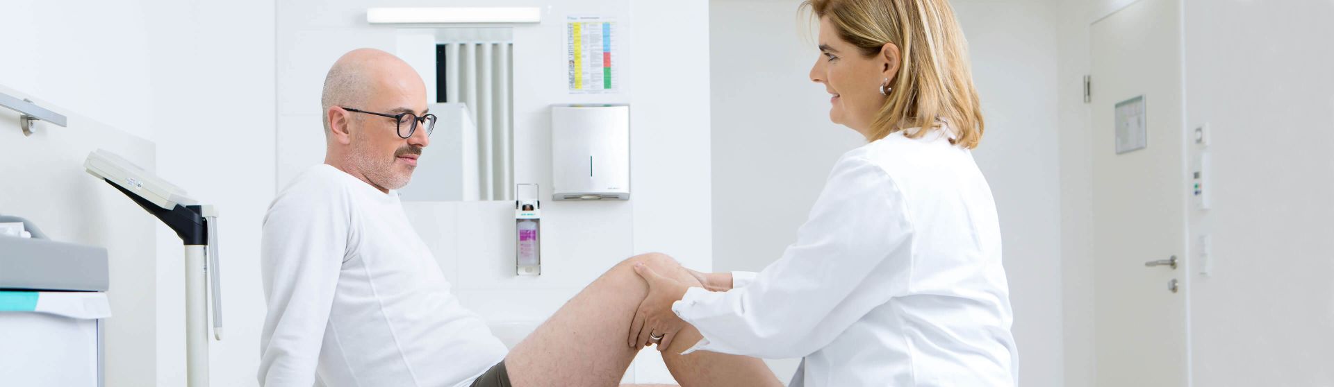 Orthopädin untersucht das Knie eines Patienten in ihrer Ordination.
